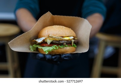 Fresh burger cooked at barbecue outdoors in craft paper. Cookout american bbq. Big hamburger with steak meat and vegetables closeup with chef unfocused at background. Street food, fast food.