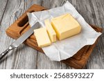 Fresh butter slices on a wooden cutting board with a butter knife, ready for spreading