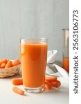 Fresh carrot juice in glass and vegetables on white table against gray background