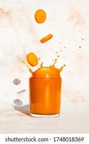 Fresh Carrot slices falling in a glass with carrot juice. splash in glass on a light background
