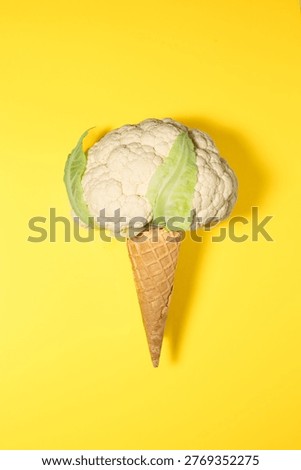Fresh cauliflower head placed inside waffle ice cream cone to look like scoop of ice cream. Set against solid, bright yellow background with clean shadows. This humorous 