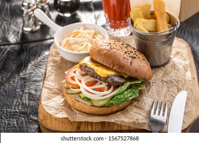 fresh cheeseburger with tomato and onion and fried potato on wooden board side view