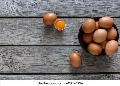 Fresh chicken brown and white home eggs with cracked eggshell and yolk in bowl at rustic wood table. Top view with copy space. Rural still life, natural healthy food and organic farming concept.
