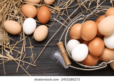 Fresh chicken eggs and dried straw on black wooden table, flat lay