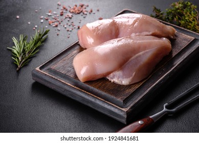 Fresh chicken fillet on a dark concrete table with spices and herbs. Preparation for cooking meat dishes