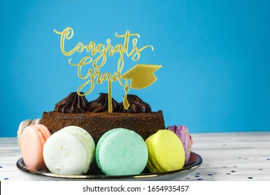 Fresh Cholocate Delicious  Cake With Maracoons Around It With Topper Congrats Grad On The Table Against Blue Background. Close Up. 