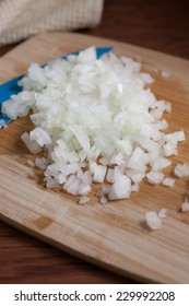 Fresh chopped onions and a blue ceramic knife on a wooden cutting board.