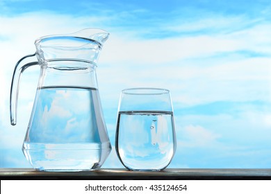 Fresh And Clean Drinking Water In Jug And Glass On Sky Background