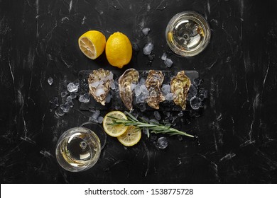 Fresh closed oysters, ice, lemon on a rectangle slate and champagne are on a black stone textured background. Top view with copy space. Close-up.