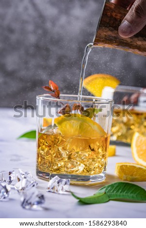 Fresh cocktail with orange, mint and ice, selective focus, Glass of the orange alcoholic drink with ice and slice of orange peel on the dark background.