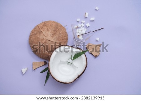 Fresh coconut chopped into dice is poured from a transparent cocktail glass on a pastel purple background. Scene for product advertising with fresh coconut ingredients.