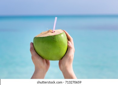 Fresh coconut cocktail in hand on turquoise sea background, travel card.