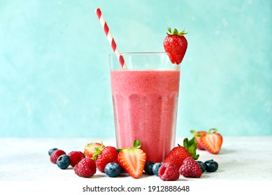 Fresh cold strawberry berry smoothie in a tall glass on a light blue slate, stone or concrete background.