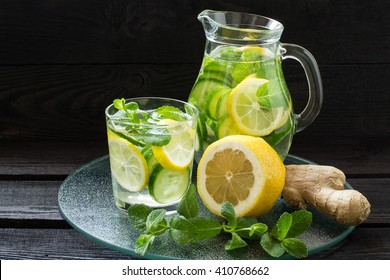 Fresh cold water with lemon, cucumber, ginger, mint and ice in a pitcher and glass on a tray