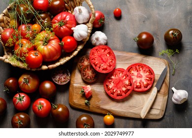 Fresh colorful ripe fall or summer heirloom variety tomatoes with knife and chopping board over wooden table background. Harvest and cooking tomato sauce concept.