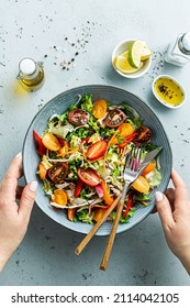 Fresh colorful spring vegetable salad with cherry tomatoes and sweet peppers. Blue bowl in woman’s hands. Healthy organic vegan lunch captured from above (top view). - Shutterstock ID 2114042105