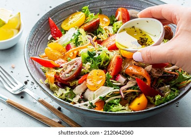 Fresh colorful spring vegetable salad with cherry tomatoes and sweet peppers in the blue bowl. Cook’s hand pouring olive oil with herbs (dressing). Healthy organic vegan lunch or snack close up. - Shutterstock ID 2120642060