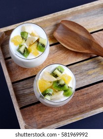 Fresh colorful vitamin breakfast, yogurt with pieces of fruits, kiwi, banana, orange, in glass cups