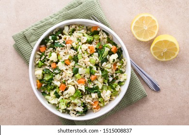 Fresh Cooked Brown Rice With Steamed Vegetables (broccoli, Cauliflower, Swiss Chard, Carrot, Celery) In Bowl, Photographed Overhead With Lemon On The Side