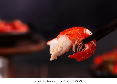 Fresh cooked crayfish with red shell and white meat held by black chopsticks against dark background, perfect for Asian cuisine and seafood dining concepts.
