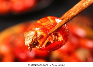 Fresh cooked crayfish tail held with chopsticks, showcasing vibrant red shell and succulent meat. Perfect for Asian cuisine, seafood restaurants, and food styling.