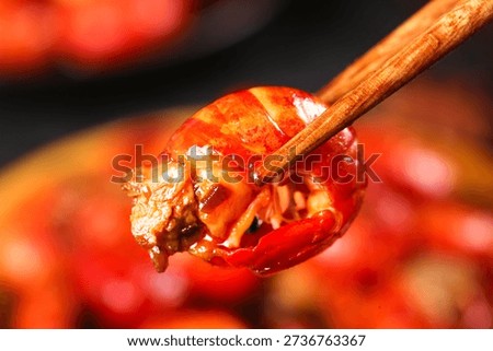 Fresh cooked crayfish tail held with chopsticks, showcasing vibrant red shell and succulent meat. Perfect for Asian cuisine, seafood restaurants, and food styling.