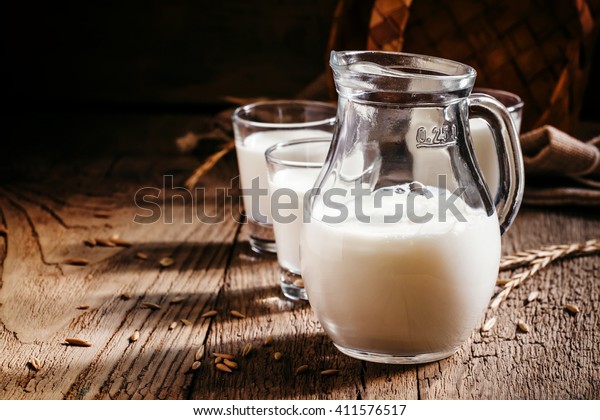 Fresh cow\'s milk in glass\
jug, vintage wooden background, still life in rustic style,\
selective focus