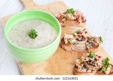 Fresh Cream Cauliflower Soup In Green Bowl With Fresh Baked Bread With Apples, Mushrooms, Cheese And Parsley On Wooden Board