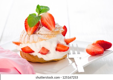 fresh cream puff with whipped cream mint and strawberries on white plate and white wood table - Powered by Shutterstock