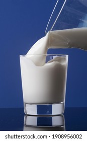 lait crémeux frais dans une carafe, versé dans un verre à la brim et isolé sur fond bleu