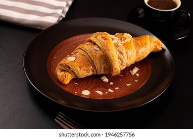 Fresh Croissant With Almond Butter In Dark Plate And Cup Of Coffee In Colored Napkin  On Black Background
