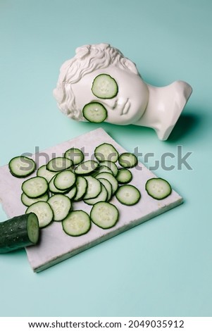 Fresh cucumber slices pattern and ancient bust with a cucumber slice mask on eyes on green background. Creative beauty concept. Spa beauty treatments at home, body care concept, organic cosmetics.