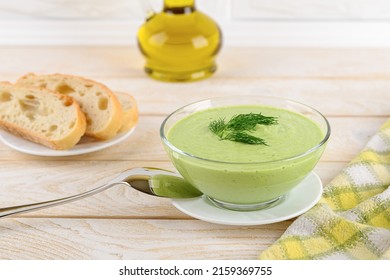 Fresh Cucumber Soup In A Glass Bowl, Spoon And Bread On A White Wooden Table. Cold Summer Vegetable Soup Of Greek Yogurt, Raw Cucumber, Avocado, Bell Pepper, Dill And Garlic. Front View.