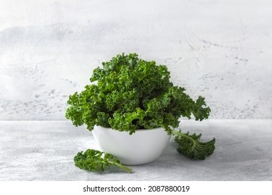 Fresh curly kale salad in a white ceramic bowl on a light gray background. Healthy eating, diet food, superfood
