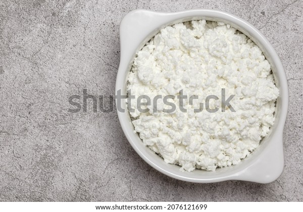 Fresh dairy farm product cottage cheese in\
ceramic bowl on a concrete background on table close-up top view.\
Healthy food containing calcium, lactose, protein, methionine,\
amino acid, vitamin,\
casein.