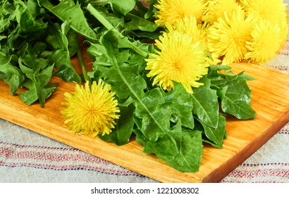 Fresh Dandelion Leaves With Flowers On Cutting Board On Table With Linen Textile, Closeup, Copy Space. Healthy Natural Organic Food Concept