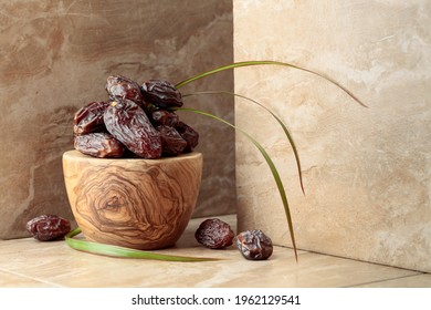 Fresh dates fruit in a wooden bowl on a beige ceramic table.