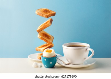 Fresh delicious breakfast with soft boiled egg, crispy toasts and cup coffee or tea on blue background. Levitation food concept. Vintage retro style - Powered by Shutterstock