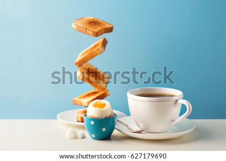 Fresh delicious breakfast with soft boiled egg, crispy toasts and cup coffee or tea on blue background. Levitation food concept. Vintage retro style