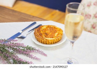 A Fresh Delicious Quiche Next To Some Orange Flowers, A Knife And Fork And A Glass Of Sparkling Wine On A White Tablecloth In A Fancy Restaurant