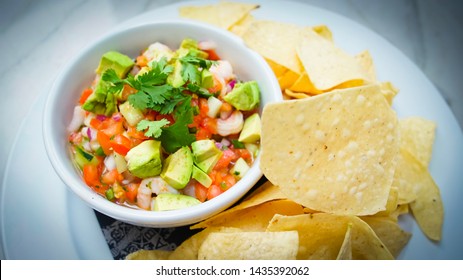 Fresh delicious shrimp ceviche with avocados tomatoes shrimp cilantro side of tortilla chips in a white bowl