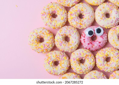Fresh donuts with icing and one cute donut with eyes, funny face on a pink background, top view