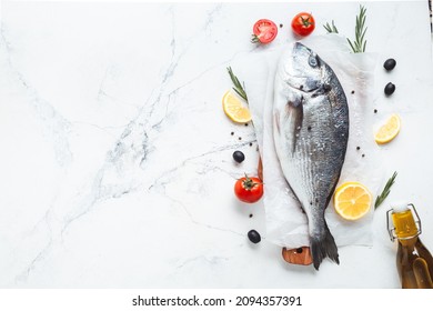 Fresh dorado fish with lemon cut, tomato, razmorin and spices on the white marble background. Flat lay fish ready to cook