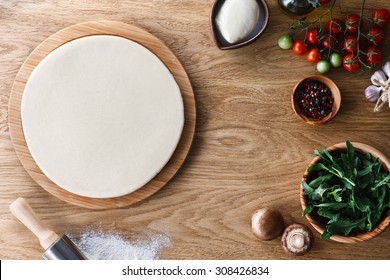 Fresh Dough Pizza Base  And Ingredients On A Wooden Textured Table. Top View.