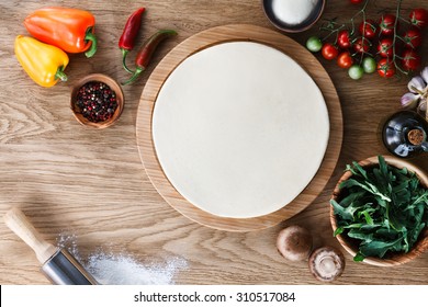 Fresh Dough Pizza Base  And Ingredients On A Wooden Textured Table. Top View.