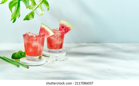 Fresh drink with watermelon and mint, cold summer lemonade, healthy mocktail. Sunny day shadows on blue sky background with copy space. Layout for wide banner. - Shutterstock ID 2117086037