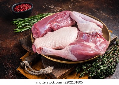 Fresh duck meat parts, raw breast steak, legs, wings in a plate with herbs. Dark background. Top view.