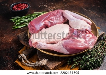 Fresh duck meat parts, raw breast steak, legs, wings in a plate with herbs. Dark background. Top view.