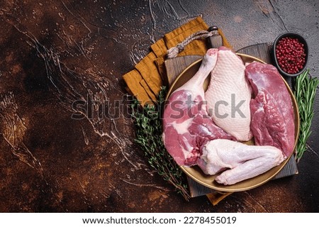 Fresh duck meat parts, raw breast steak, legs, wings in a plate with herbs. Dark background. Top view. Copy space.