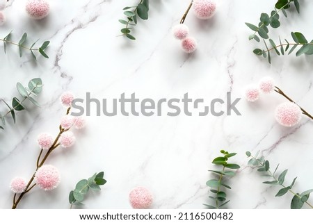 Fresh eucalyptus leaves, twigs with pink fluffy balls. Winter flat lay background, copy-space. Top view on off white marble table.
